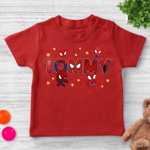 Puede incluir: Camiseta roja con el nombre "TOMMY" en estilo c&oacute;mic, con gr&aacute;ficos de Spider-Man. El dise&ntilde;o incluye personajes de Spider-Man, telara&ntilde;as y estrellas amarillas. Una camiseta divertida y colorida para ni&ntilde;os.