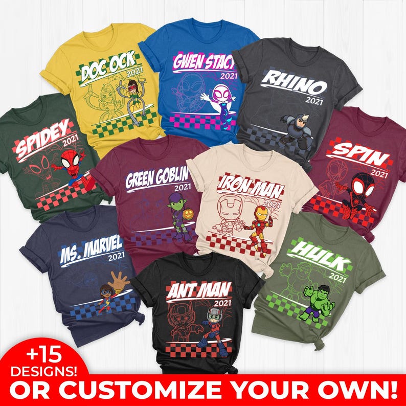 May include: A collection of colorful t-shirts featuring various superhero characters and logos. Each shirt displays a character name and the year "2021". The shirts are in various colors, including green, yellow, blue, and black, with graphic designs.