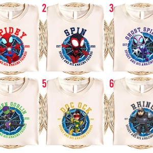 Puede incluir: Seis camisetas color crema con diferentes dise&ntilde;os de superh&eacute;roes. Cada camiseta presenta el nombre de un personaje en un c&iacute;rculo con un dise&ntilde;o de telara&ntilde;a y el texto "Spidey and His Amazing Friends". Los personajes incluyen Spidey, Spin, Ghost Spider, Green Goblin, Doc Ock y Rhino.