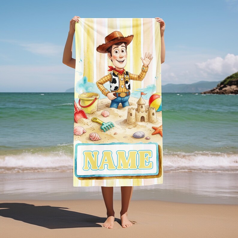May include: A rectangular beach towel featuring a cartoon cowboy character wearing a brown hat, yellow shirt, and cow-print vest. The design includes a sandcastle, beach toys, seashells, and a rectangular box with the word NAME in yellow text.