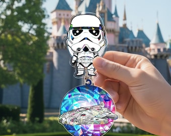 May include: A clear acrylic keychain featuring a cartoon Stormtrooper and a Millennium Falcon design. The keychain has a blue ring and a colorful, geometric background. The background includes shades of blue, purple, pink, and green.