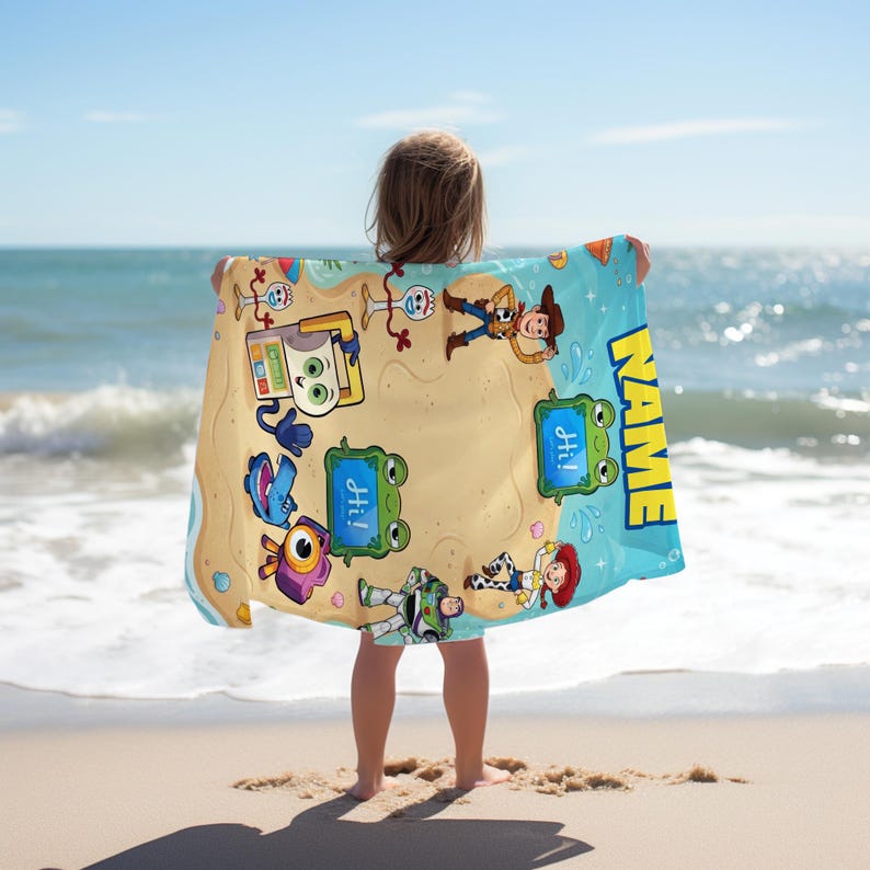 May include: A beach towel featuring cartoon characters on a sandy beach design with a blue border. The towel has the word "NAME" in yellow and the word "Hi!" in blue speech bubbles. The towel is held by a person on a sandy beach with the ocean in the background.
