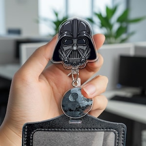 May include: A black and gray retractable badge holder featuring Darth Vader's helmet and a Death Star graphic. The badge holder is attached to a black leather-like card holder.