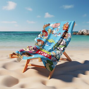 May include: A light blue beach towel featuring a colorful print of various animated characters and the text DANIEL STORY in yellow and white letters. The towel is draped over a wooden beach chair, showcasing a repeating pattern of cartoon figures.