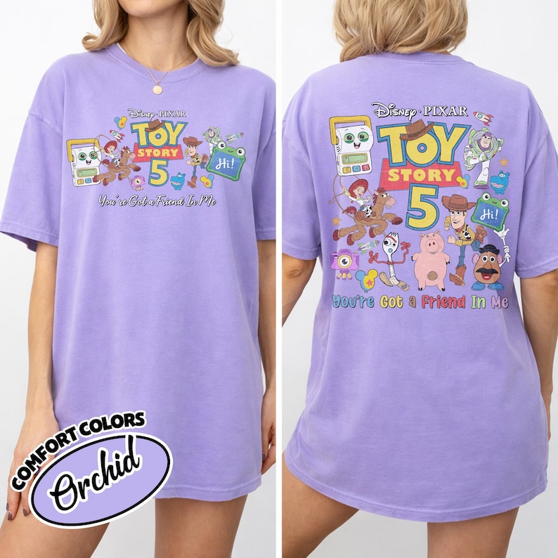 May include: A lilac-colored t-shirt featuring the Toy Story 5 logo and characters. The front of the shirt displays the logo and characters, while the back has a larger design with the text "You've Got a Friend In Me."