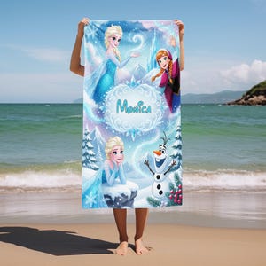 May include: A beach towel featuring characters from the animated film Frozen. The towel has images of Elsa, Anna, and Olaf, with the name "Monica" in a decorative font. The background includes snowflakes, mountains, and a castle.