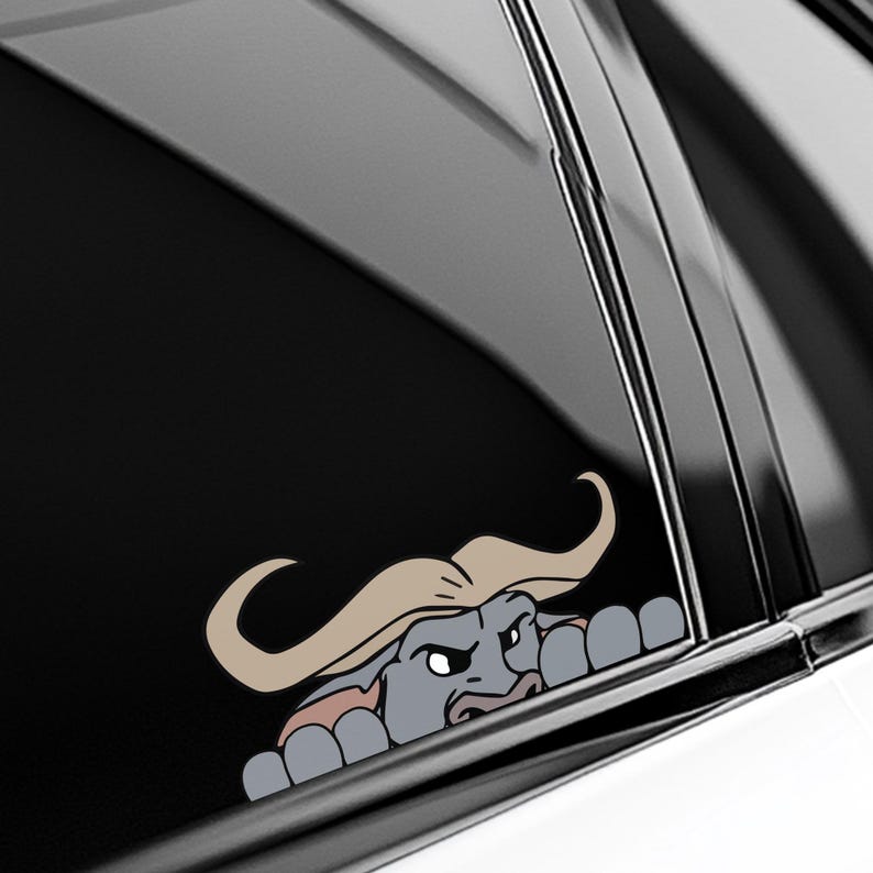 May include: A cartoon-style decal of a buffalo peeking over a surface. The buffalo has a gray body, tan hair, and an angry expression. The decal is designed to be applied to a car window or similar surface.