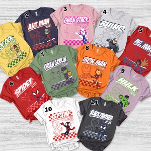 May include: A collection of eleven colorful t-shirts featuring various Marvel characters. Each shirt displays a character's name and the year 2021, along with a corresponding graphic design. The shirts are arranged in a circular pattern.