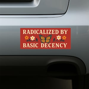 May include: A rectangular bumper sticker with the text "RADICALIZED BY BASIC DECENCY" in white. The sticker has a red background and features a butterfly and floral design in orange, yellow, and green.