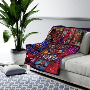 May include: A blue, red, and white Spider-Man themed throw blanket. The blanket features comic book panels and images of Spider-Man. The name "PERCY" is printed in red on the blanket. The blanket is draped over a white couch.