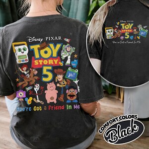 May include: Black t-shirt featuring a colorful graphic of Toy Story characters and the text "Toy Story 5". The design includes Woody, Buzz Lightyear, and other characters from the movie. The phrase "You're Got a Friend In Me" is also included.