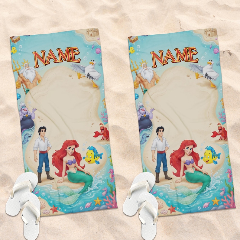 May include: Two rectangular beach towels featuring a printed scene with Ariel, Prince Eric, King Triton, Ursula, Flounder, and Sebastian. The design includes a sandy beach, ocean water, and the word NAME at the top. Two pairs of white flip-flops.