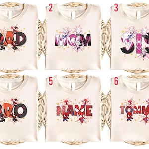 Puede incluir: Camisetas de color crema con varios dise&ntilde;os que muestran las palabras "DAD", "MOM", "SIS", "BRO", "NAME" y "TOMMY". Cada dise&ntilde;o incluye personajes de Spider-Man, telara&ntilde;as y detalles de estrellas. Las camisetas se exhiben sobre una superficie tejida.