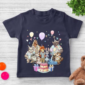 May include: Navy blue toddler t-shirt featuring a colorful birthday party scene with cartoon animal characters, balloons, and a cake. The number "3" is displayed on a balloon. The shirt has a crew neck and short sleeves.