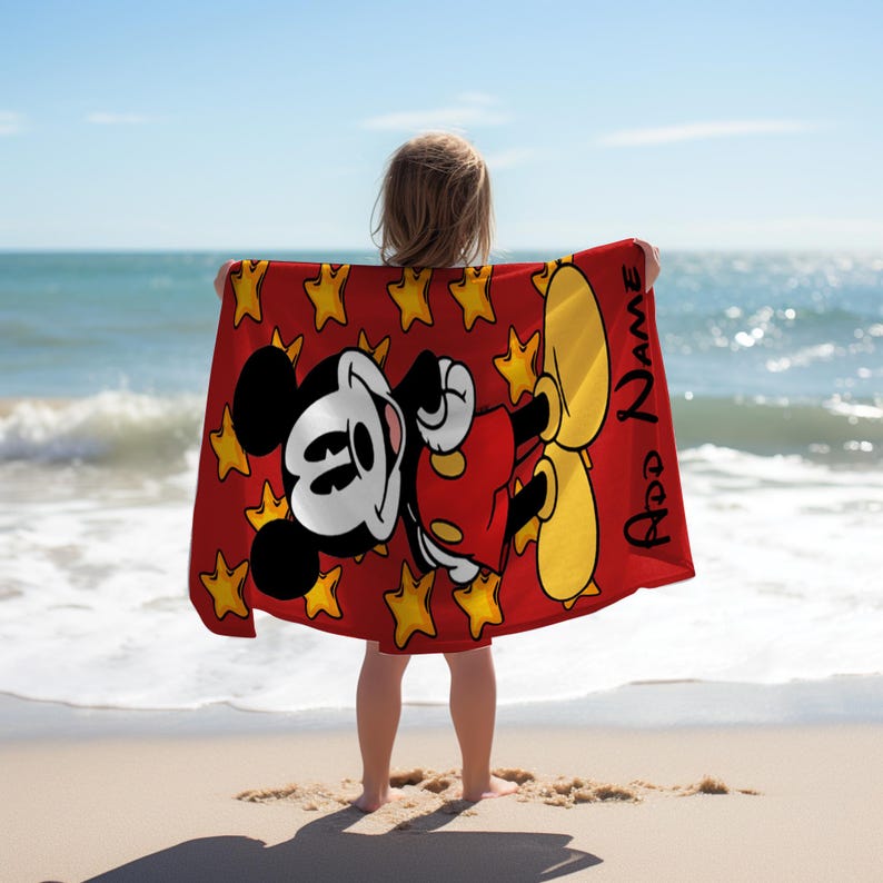May include: A rectangular beach towel featuring a red background with a repeating pattern of yellow stars and a large graphic of Mickey Mouse wearing red shorts and yellow shoes. The text "Add Name" is printed vertically in black on the right side.