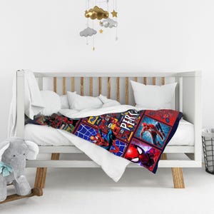 May include: A Spider-Man themed baby blanket with a colorful design. The blanket features various action poses of Spider-Man in a grid pattern against a blue and red background. The blanket is draped over a white crib.