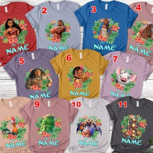 K&ouml;nnte beinhalten: Elf kurz&auml;rmelige T-Shirts in verschiedenen Farben, jeweils mit einer Figur aus einem beliebten Animationsfilm. Jedes Shirt hat ein Charakterbild, das von einem Blumengirlande umgeben ist, und darunter das Wort "NAME".