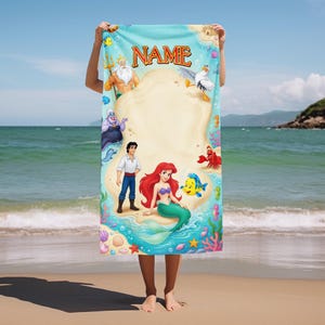 May include: A rectangular beach towel featuring a light blue background with a central sandy area and the text NAME at the top. The design includes illustrations of Ariel, Prince Eric, King Triton, Ursula, Flounder, Sebastian, and Scuttle.