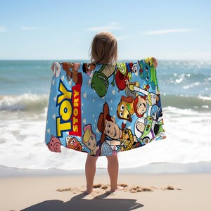 Puede incluir: Una toalla de playa rectangular con fondo azul claro y un estampado colorido de varios personajes de Toy Story, incluyendo a Woody, Buzz Lightyear y Bo Peep, junto al logotipo rojo y amarillo de Toy Story en el lado izquierdo.