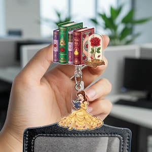 May include: A badge reel featuring a stack of colorful books, a rose in a glass dome, and a cartoon of a woman in a yellow dress reading a book. The reel is attached to a black card holder.