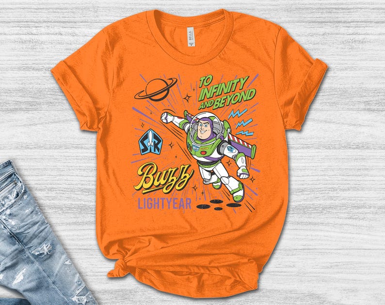 May include: An orange short-sleeve t-shirt featuring a graphic of Buzz Lightyear in flight. The design includes the text "TO INFINITY AND BEYOND", "Buzz", and "LIGHTYEAR", along with a planet icon and a space ranger emblem in blue, green, and purple.