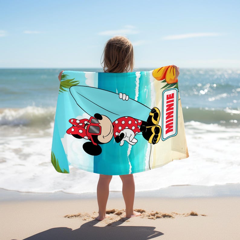May include: A rectangular beach towel featuring a graphic of Minnie Mouse wearing red sunglasses and a red polka dot outfit while holding a light blue surfboard. The design includes palm leaves, a beach scene, and the text MINNIE in a white box.