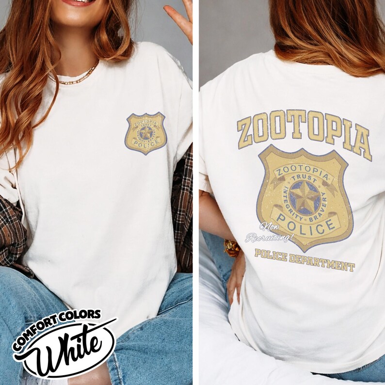 Puede incluir: Camiseta blanca con una insignia del Departamento de Polic&iacute;a de Zootopia en la parte delantera y trasera. La insignia delantera es m&aacute;s peque&ntilde;a, mientras que la trasera muestra el logotipo de Zootopia y las palabras "Integridad, Valent&iacute;a, Confianza". La camiseta tiene las palabras "Comfort Colors" y "White".