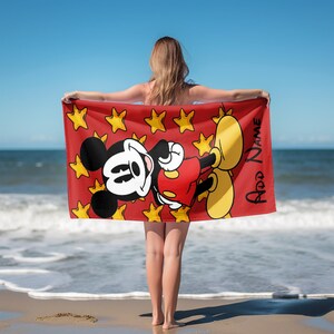 May include: A rectangular beach towel featuring a red background with a pattern of yellow stars and a large graphic of Mickey Mouse. The character is depicted in black, white, and red with yellow shoes. The text Add Name is printed in black.