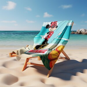 May include: A beach towel draped over a wooden lounge chair featuring a graphic of Minnie Mouse wearing red polka-dot sunglasses and a matching shirt while surfing. The towel displays the name MINNIE in red letters and large yellow hibiscus flowers.