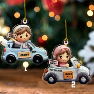 May include: Two car-shaped Christmas ornaments. One is light blue with the name "Johnson" and the text "learner's PERMIT" on a sign. The other is white with the name "Lisana" and the text "learner's PERMIT" and "clear the road!" on a sign.