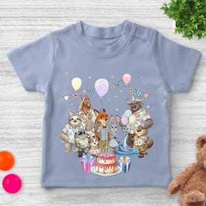 May include: A light blue toddler t-shirt featuring a colorful birthday party scene with cartoon animal characters. The number "3" is displayed on a balloon, and a birthday cake is also visible.