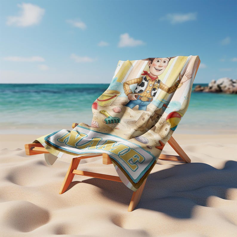 May include: A beach towel draped over a wooden beach chair, featuring a cartoon cowboy character, a sandcastle, a bucket, and a shovel on a sandy background. The word NAME is printed in large, bold, light-coloured letters at the bottom edge.