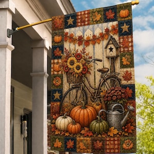 May include: A rectangular garden flag featuring a quilted-style border of autumn leaves, pumpkins, and stars. The center depicts a bicycle with a basket of sunflowers, a wooden birdhouse, pumpkins, a metal watering can, and fall foliage.