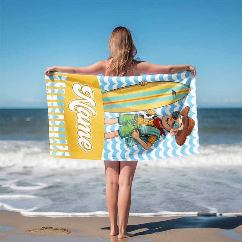 May include: A rectangular beach towel featuring a yellow vertical panel with the word Name in white script. The main section displays a cartoon character wearing a brown hat and sunglasses, holding a yellow and blue surfboard over a blue wave pattern.