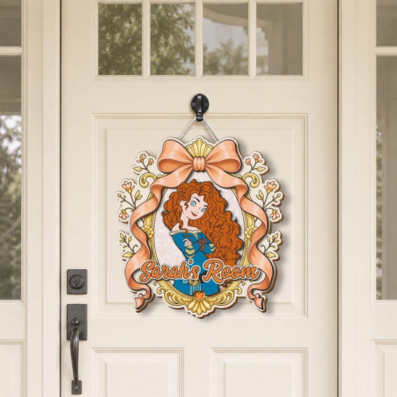 May include: A decorative wooden door sign featuring a cartoon illustration of a girl with long curly red hair wearing a blue dress. The sign is framed by a gold border and a large peach-colored bow, with the text Sarah's Room written in orange.