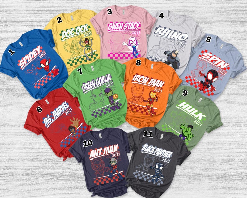 May include: A collection of eleven short-sleeved t-shirts in various colors, each featuring a different superhero graphic and the year 2021. The shirts include characters like Spidey, Ms. Marvel, Doc Ock, Gwen Stacy, Rhino, Spin, Iron Man, Hulk, Ant Man, and Black Panther.