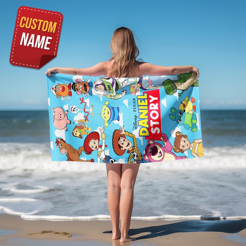 May include: A light blue beach towel featuring a colorful print of various Toy Story characters, including Woody, Buzz Lightyear, and Jessie, with the text DANIEL STORY prominently displayed in a red and yellow vertical graphic design.