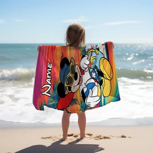 May include: A rectangular beach towel featuring a colorful sunset background with palm tree silhouettes. The towel displays a cartoon mouse wearing sunglasses and holding a beach ball, with the word Name printed vertically in white text.