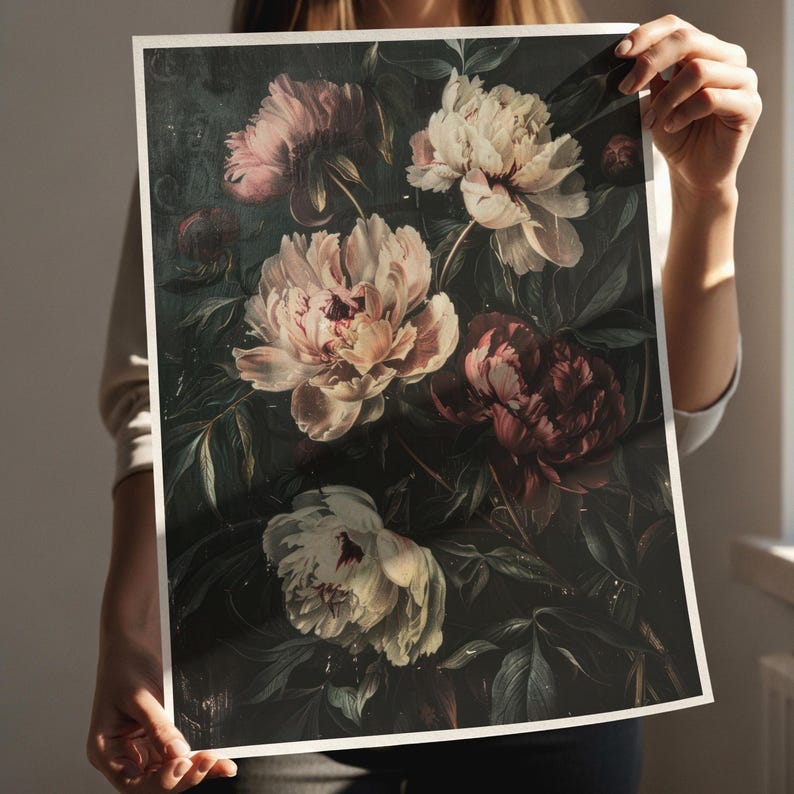 May include: A floral print featuring a dark background with large, detailed peony blooms in shades of pink, cream, and burgundy. The artwork has a vintage aesthetic, with visible brushstrokes and a moody, romantic feel. The print is held by a person.