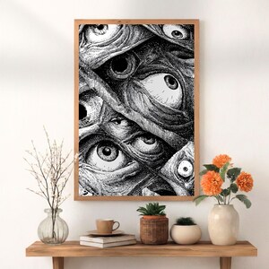 May include: A framed black and white print featuring a detailed illustration of numerous eyes. The artwork is set in a wooden frame and displayed on a wooden shelf with decorative items, including flowers and plants.