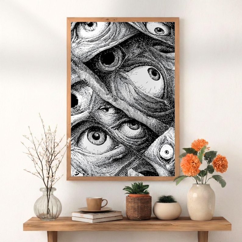 May include: A framed black and white print featuring a detailed illustration of numerous eyes. The artwork is set in a wooden frame and displayed on a wooden shelf with decorative items, including flowers and plants.