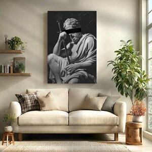May include: Black and white canvas art print of a classical statue holding a sword, with a black bar obscuring the eyes. The artwork is displayed above a cream-colored sofa in a living room setting.