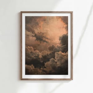May include: Framed art print featuring a dramatic cloudscape in shades of brown, gray, and peach. The artwork depicts a detailed view of layered clouds, with light filtering through, creating a moody and atmospheric scene. The print is encased in a wooden frame.
