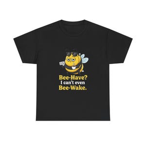May include: Black t-shirt featuring a cartoon bee wearing sunglasses and holding a coffee cup. The bee has a tired expression and the text reads "Bee-Have? I can't even Bee-Wake."