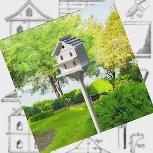 May include: A white birdhouse with a gray shingled roof, mounted on a tall gray pole. The birdhouse has multiple openings and is surrounded by lush green trees and grass. The background includes architectural sketches.