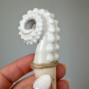 May include: White ceramic octopus bottle stopper with a cork base and twine wrapped around the cork.