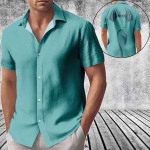 May include: A short-sleeved button-down shirt in a solid teal colour. The front features a classic collar and a button placket. An inset circle shows the back of the shirt, which displays a graphic of dark wings and a pointed tail in the centre.