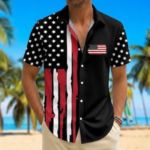 Puede incluir: Una camisa de manga corta con botones y diseño dividido. El lado izquierdo muestra un fondo negro con estrellas blancas y rayas verticales rojas y blancas. El lado derecho es negro sólido con un pequeño gráfico de la bandera de EE. UU. en el pecho.