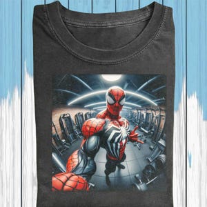 May include: Dark gray t-shirt featuring a graphic of Spider-Man in a gym setting. The superhero is in a red and black suit, striking a pose. The background shows gym equipment and bright lights.