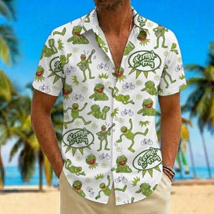 May include: A white short-sleeved button-down shirt featuring an all-over green print of Kermit the Frog in various poses, including playing a banjo and riding a bicycle, interspersed with the text Kermit the Frog in circular green emblems.